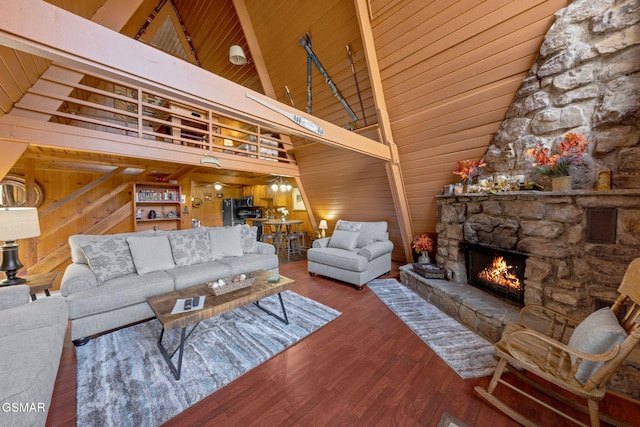 living room with high vaulted ceiling, wood finished floors, wooden walls, a stone fireplace, and wood ceiling
