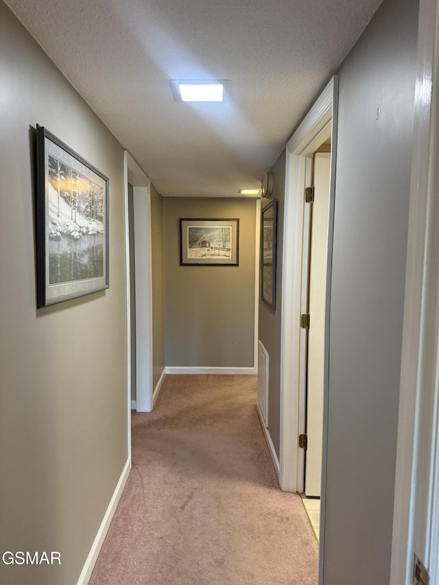 corridor featuring light carpet, baseboards, and a textured ceiling