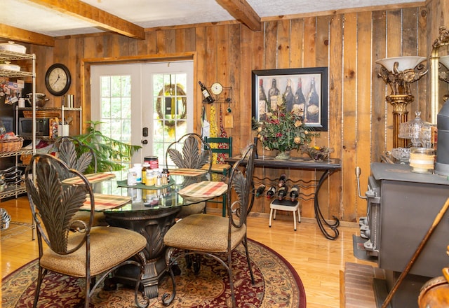 dining room with beam ceiling, wood walls, french doors, and hardwood / wood-style floors