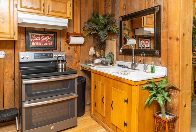 kitchen with stainless steel electric range oven, sink, wood walls, and light wood-type flooring