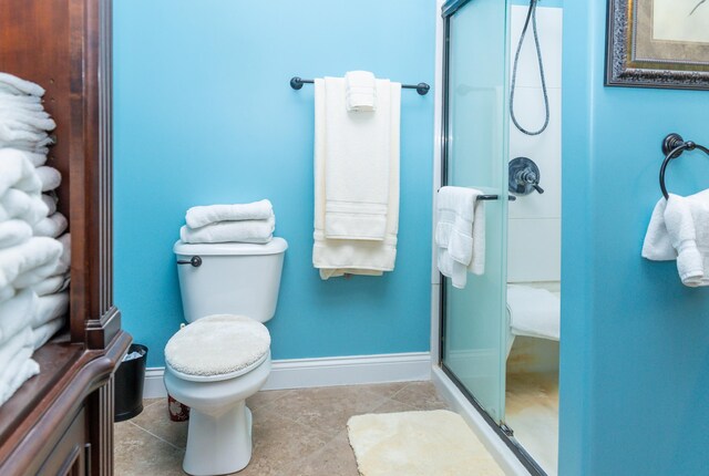 bathroom with tile patterned floors, toilet, and a shower with door