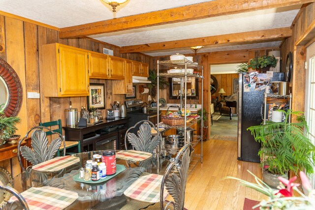 dining room with beam ceiling, wooden walls, and light hardwood / wood-style flooring