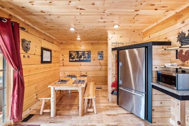 kitchen with wood ceiling, wooden walls, light wood-type flooring, and appliances with stainless steel finishes
