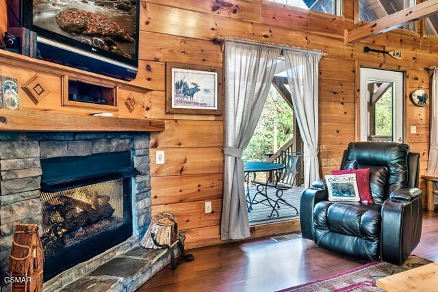 living area featuring a stone fireplace, wood walls, lofted ceiling with beams, and dark hardwood / wood-style floors