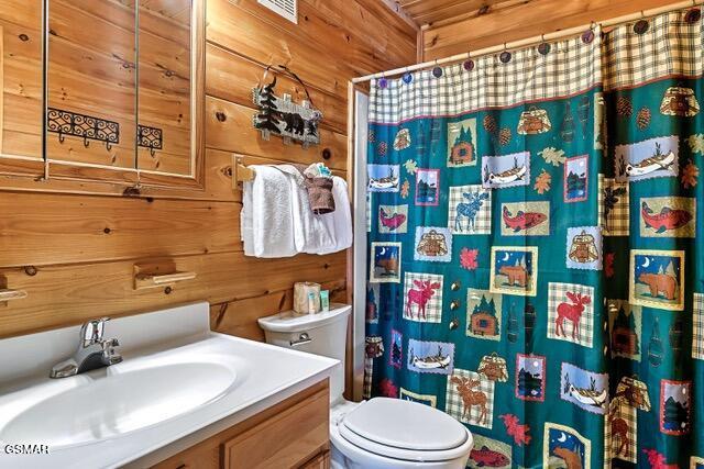 bathroom with vanity, wood walls, toilet, and walk in shower