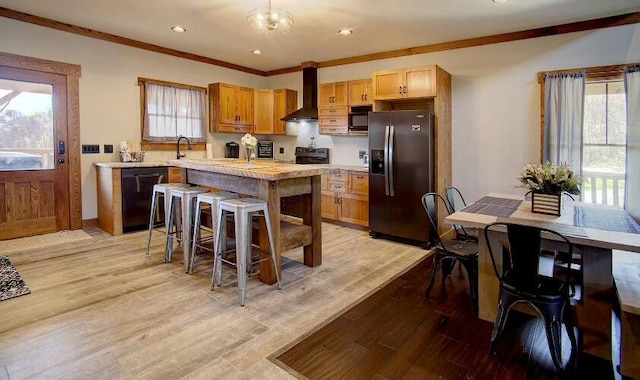 kitchen featuring light hardwood / wood-style flooring, black appliances, wall chimney range hood, and ornamental molding