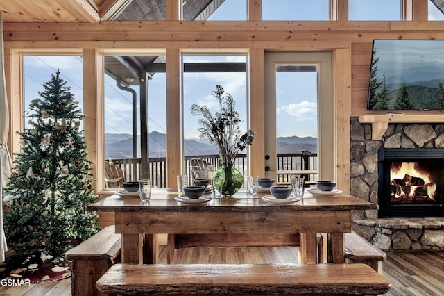 dining area featuring hardwood / wood-style flooring, a stone fireplace, and wood walls