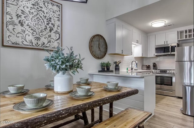 kitchen featuring a peninsula, a sink, light countertops, appliances with stainless steel finishes, and decorative backsplash