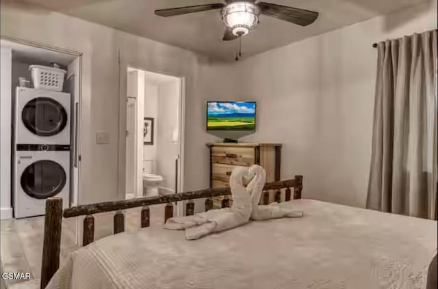 bedroom featuring wood finished floors, stacked washing maching and dryer, ensuite bath, and a ceiling fan