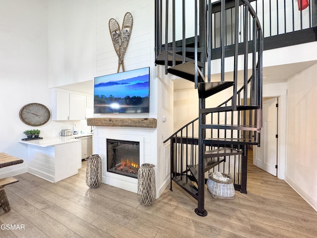 stairway featuring a glass covered fireplace, baseboards, a high ceiling, and wood finished floors