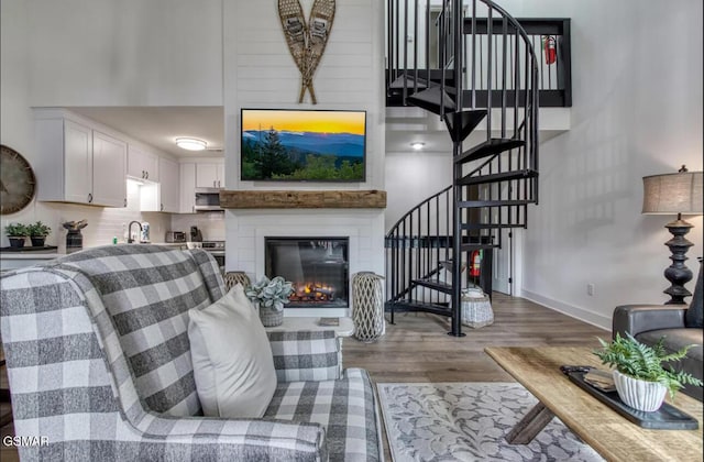 living area with wood finished floors, a towering ceiling, baseboards, stairway, and a glass covered fireplace