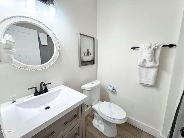 half bathroom featuring vanity, wood finished floors, toilet, and baseboards