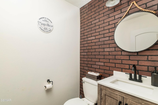 bathroom featuring toilet, brick wall, and vanity