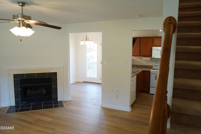 unfurnished living room with stairs, a tile fireplace, wood finished floors, and baseboards