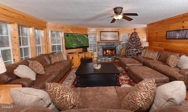 living room with wooden walls, a fireplace, ceiling fan, and a textured ceiling