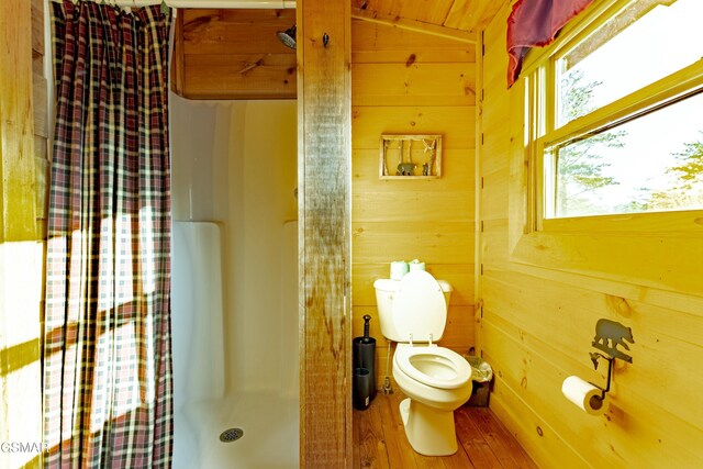 bathroom featuring toilet, a stall shower, wood finished floors, wood walls, and lofted ceiling