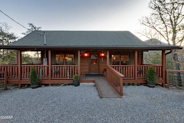 back of house featuring covered porch and a shingled roof