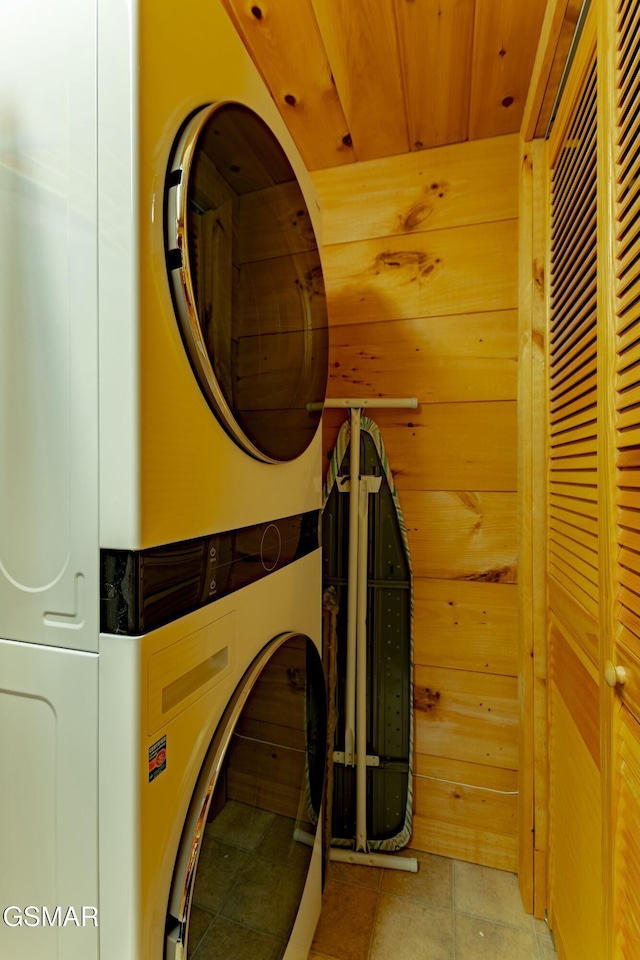 laundry room with light tile patterned floors, wood walls, stacked washer and clothes dryer, and wood ceiling