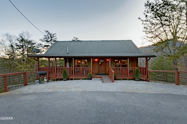 rustic home featuring covered porch, a shingled roof, and fence