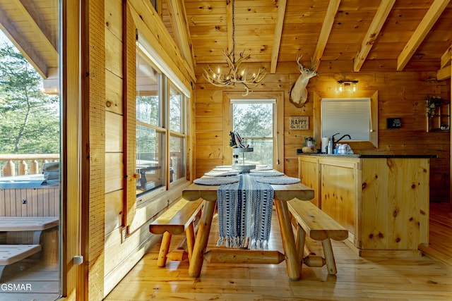 dining area with light wood finished floors, an inviting chandelier, lofted ceiling with beams, wood ceiling, and wood walls