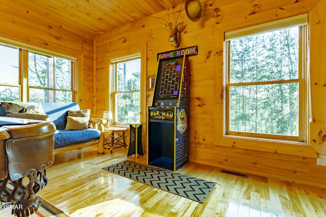 living area featuring hardwood / wood-style flooring, wooden walls, wood ceiling, and visible vents