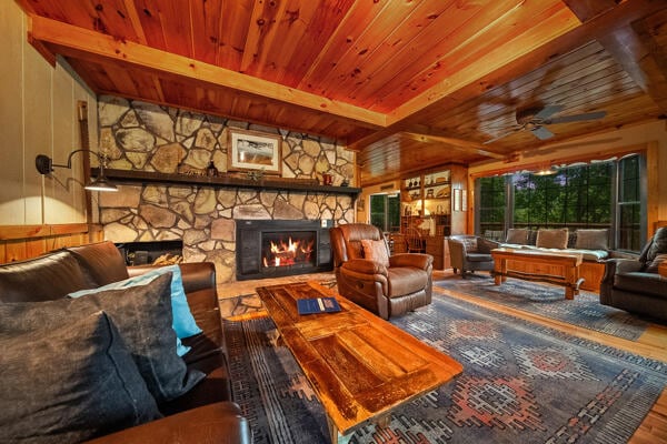 living room featuring beam ceiling, ceiling fan, hardwood / wood-style floors, wooden walls, and a fireplace