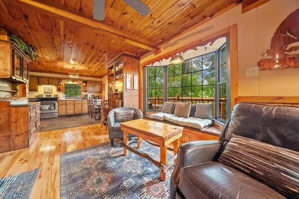 living room featuring wooden walls, light hardwood / wood-style flooring, ceiling fan, beam ceiling, and wood ceiling