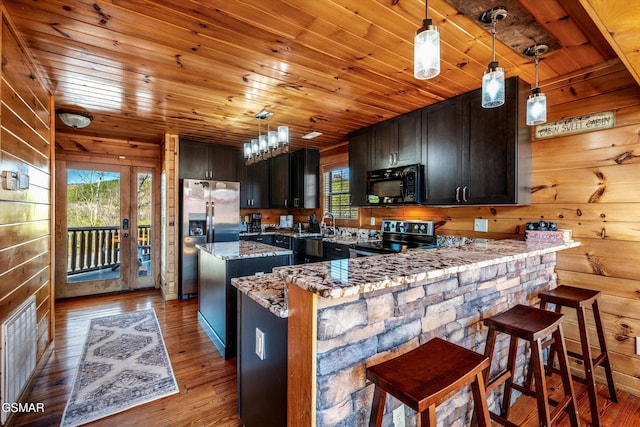 kitchen featuring light stone counters, wooden walls, a peninsula, appliances with stainless steel finishes, and wood-type flooring