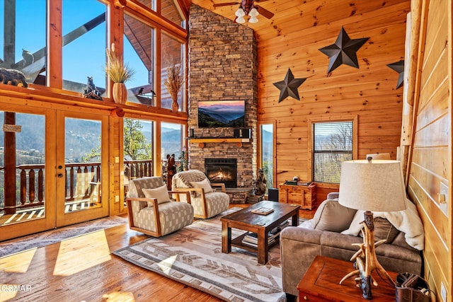 living area featuring ceiling fan, hardwood / wood-style flooring, wood walls, a fireplace, and french doors