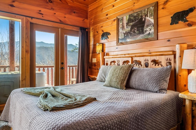 bedroom with access to outside, multiple windows, a mountain view, and wooden walls