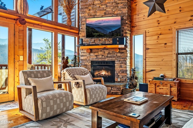 living area with a high ceiling, wooden walls, an outdoor stone fireplace, and hardwood / wood-style floors