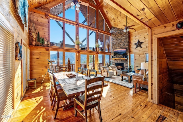 dining room with wood ceiling, wood walls, a stone fireplace, and hardwood / wood-style floors