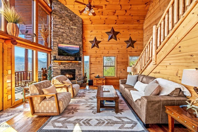 living room with a stone fireplace, stairway, hardwood / wood-style floors, and wooden walls