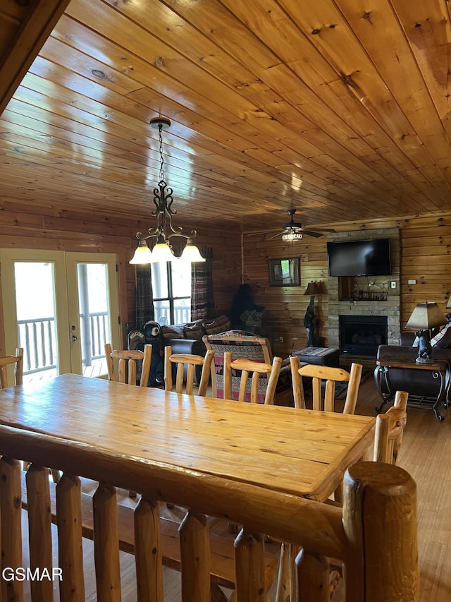 dining room with wood finished floors, a fireplace, ceiling fan, wooden walls, and wooden ceiling