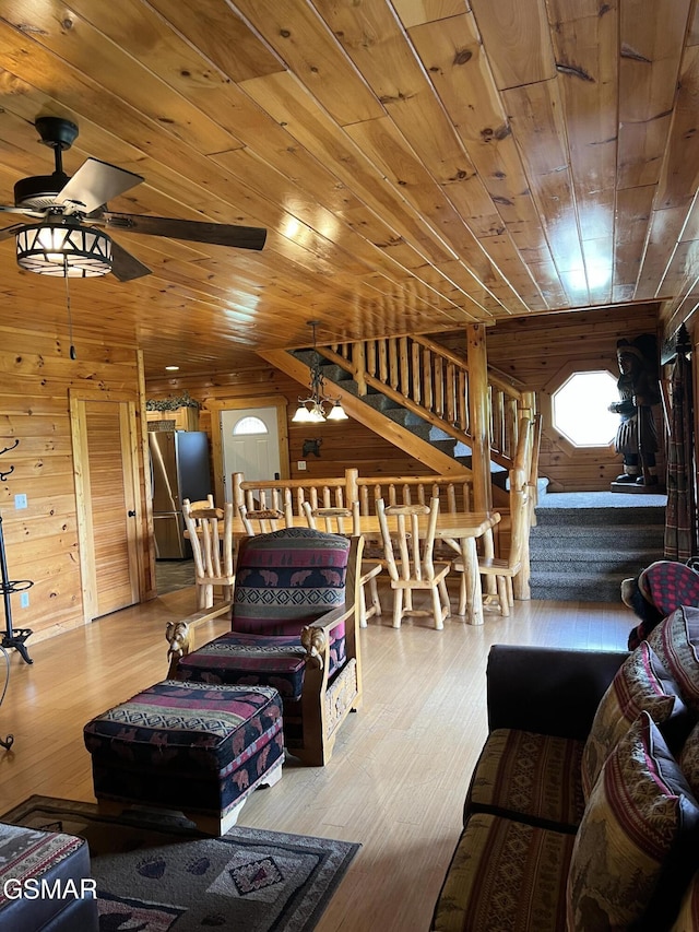 living area featuring wood ceiling, wood walls, ceiling fan, and stairs