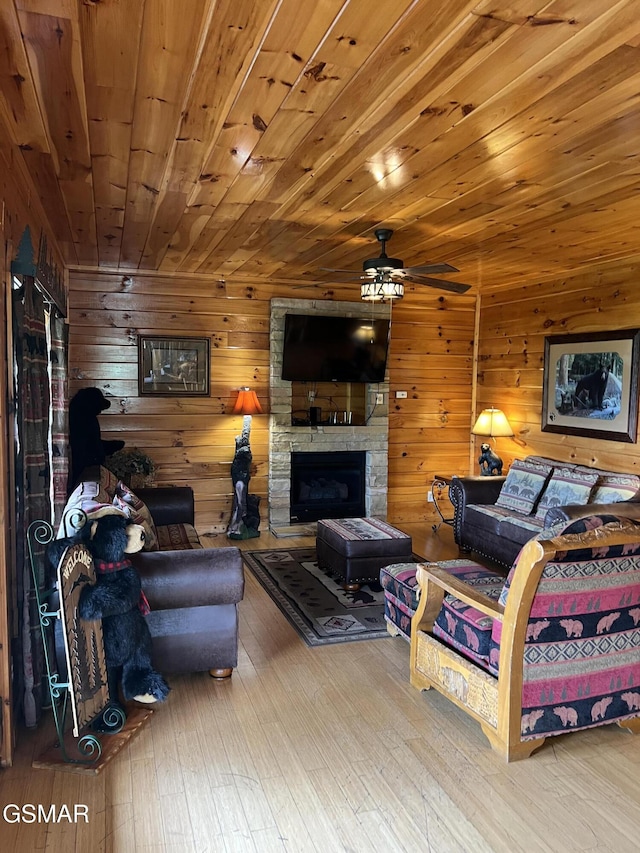 living area featuring hardwood / wood-style flooring, wooden walls, a fireplace, and a ceiling fan