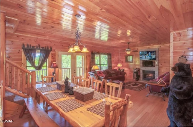 dining space with wood ceiling, wood walls, a lit fireplace, wood finished floors, and stairway