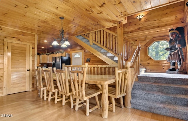unfurnished dining area with a chandelier, wooden walls, stairs, and light wood-style floors