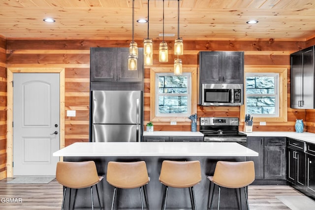 kitchen featuring wood walls, light countertops, appliances with stainless steel finishes, wooden ceiling, and a kitchen breakfast bar