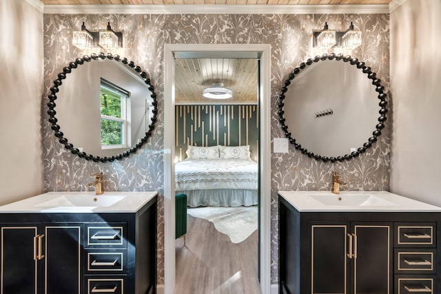 ensuite bathroom featuring crown molding, two vanities, a sink, and wallpapered walls