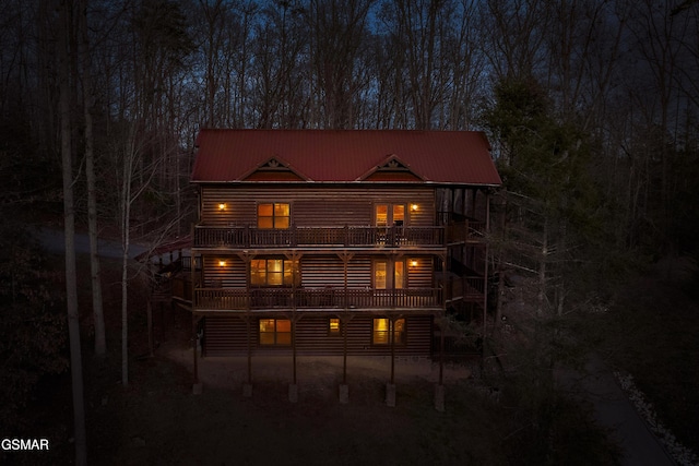 back of house featuring faux log siding, metal roof, and a balcony