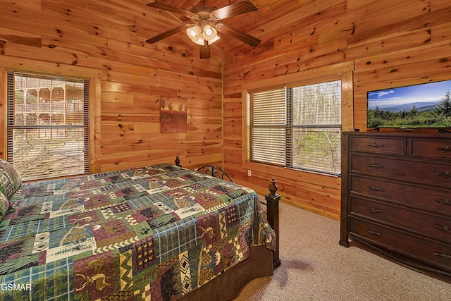 bedroom with light colored carpet, wood walls, a ceiling fan, and multiple windows
