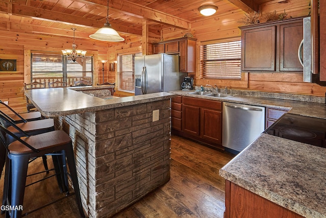 kitchen with a sink, appliances with stainless steel finishes, dark wood-style floors, and wood walls