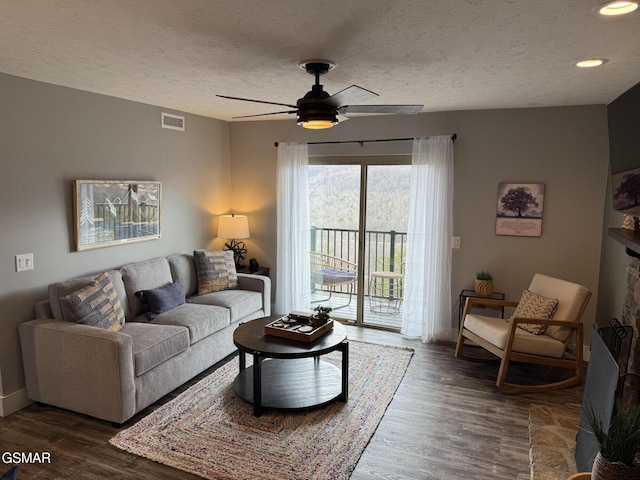 living area with a textured ceiling, dark wood-style flooring, ceiling fan, and visible vents