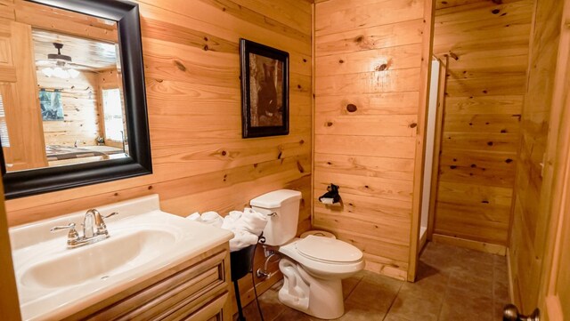 bathroom with tile patterned floors, vanity, ceiling fan, wooden walls, and toilet