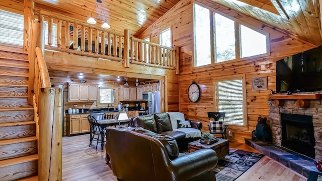 living room featuring light wood-type flooring, high vaulted ceiling, wooden ceiling, a stone fireplace, and wood walls