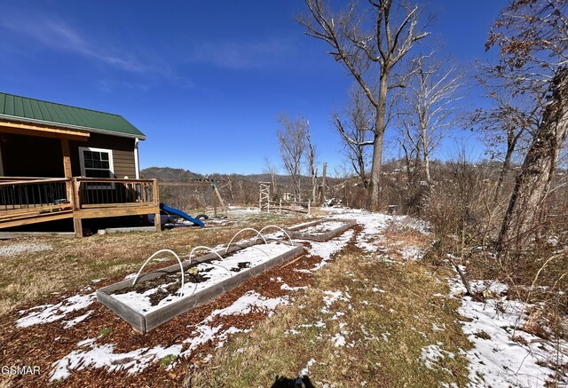 yard layered in snow with a playground and a wooden deck