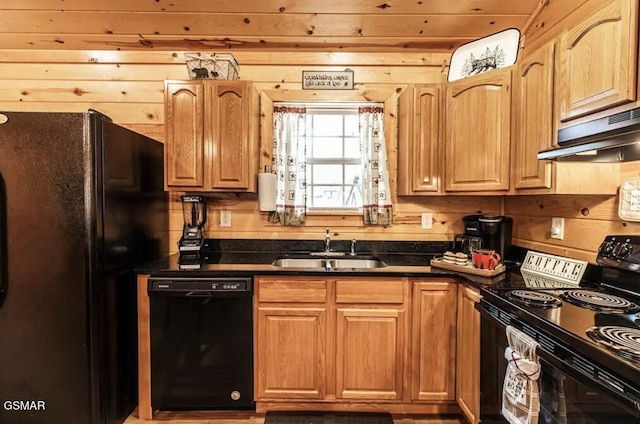 kitchen featuring dark countertops, a sink, wood walls, under cabinet range hood, and black appliances