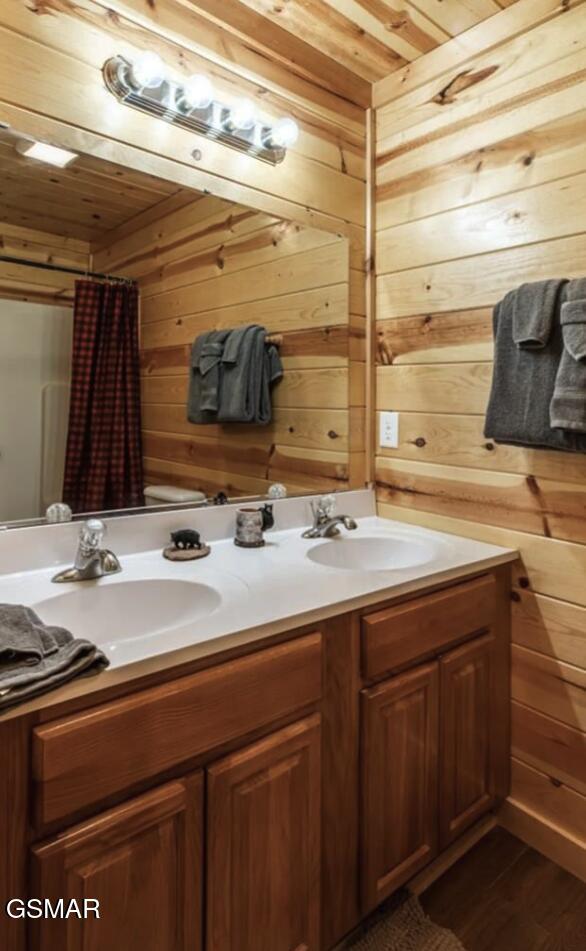 full bath with double vanity, wood walls, a sink, and wooden ceiling