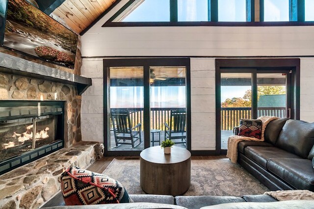 living room featuring wood ceiling, wooden walls, high vaulted ceiling, hardwood / wood-style floors, and a stone fireplace